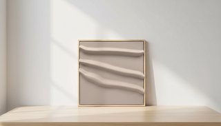 Square minimalist artwork with sculptural, wave-like relief textures in soft beige tones, set in a light wood frame and illuminated by gentle natural sunlight.